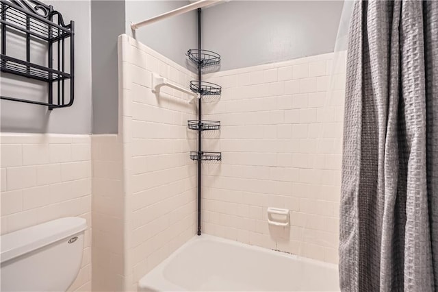 bathroom with toilet, wainscoting, shower / bath combination with curtain, and tile walls