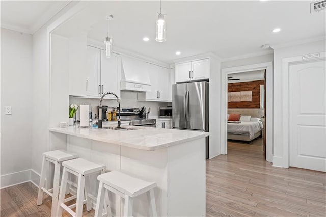 kitchen featuring appliances with stainless steel finishes, white cabinets, decorative light fixtures, custom exhaust hood, and kitchen peninsula