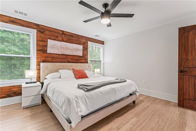 bedroom with crown molding, ceiling fan, multiple windows, and wood walls