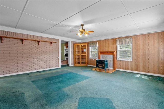 6674 Cowan Mill Rd, Winston, GA 30187 - unfurnished living room featuring a wood stove, carpet flooring, brick wall, a ceiling fan, and wooden walls