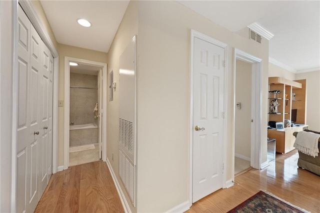 hall featuring light wood-style floors, visible vents, ornamental molding, and baseboards