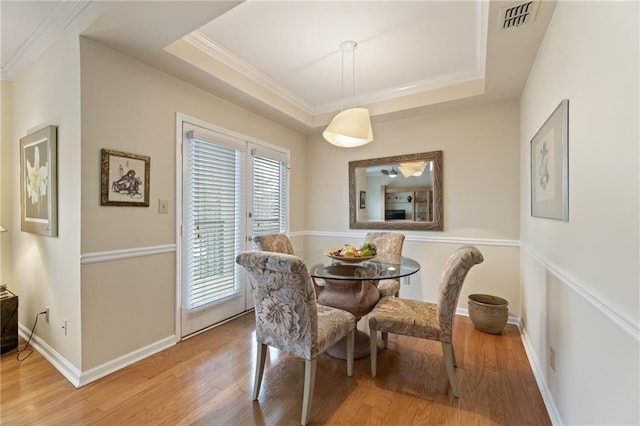 dining space with light wood-type flooring, a raised ceiling, and visible vents