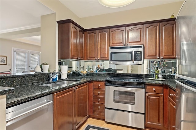 kitchen with light wood-style flooring, dark stone countertops, a peninsula, stainless steel appliances, and a sink