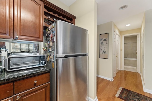 kitchen with a toaster, baseboards, dark stone countertops, freestanding refrigerator, and light wood-style floors