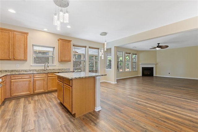 kitchen with hardwood / wood-style floors, light stone countertops, a center island, and pendant lighting