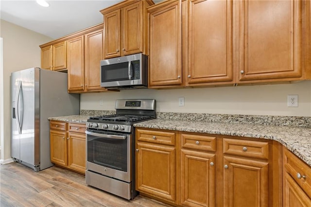 kitchen featuring appliances with stainless steel finishes, light stone countertops, and light wood-type flooring