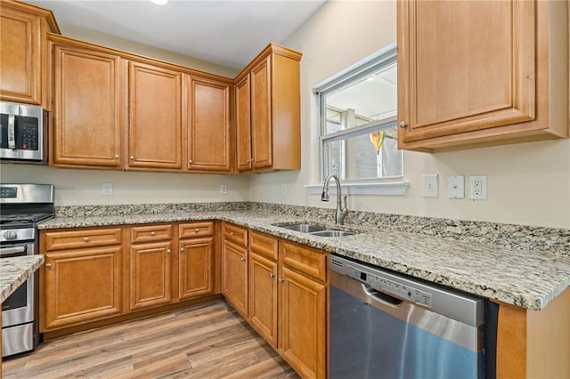 kitchen with appliances with stainless steel finishes, sink, light stone counters, and light hardwood / wood-style floors