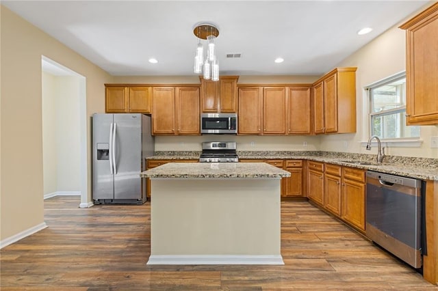 kitchen with appliances with stainless steel finishes, light hardwood / wood-style flooring, sink, pendant lighting, and a center island