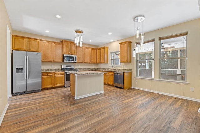 kitchen with hardwood / wood-style floors, light stone countertops, a center island, decorative light fixtures, and appliances with stainless steel finishes