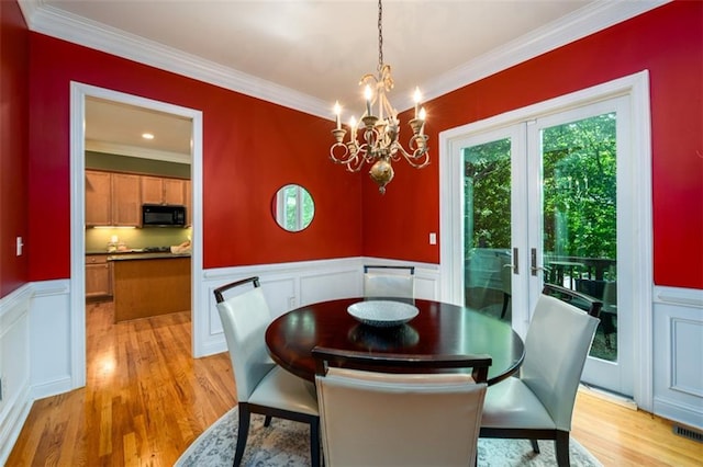 dining room featuring ornamental molding, a decorative wall, wainscoting, light wood-style floors, and a chandelier