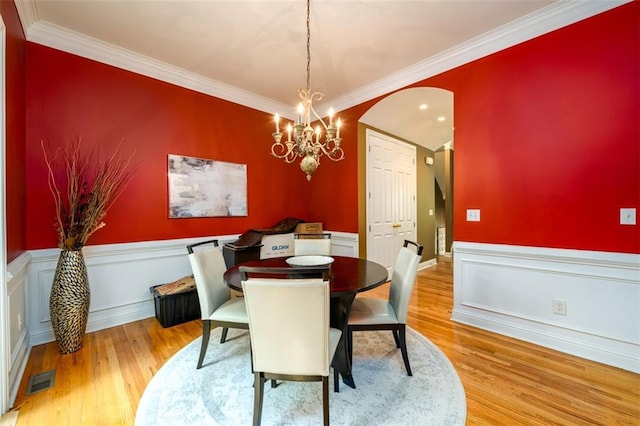dining space featuring wood finished floors, arched walkways, a wainscoted wall, a chandelier, and crown molding