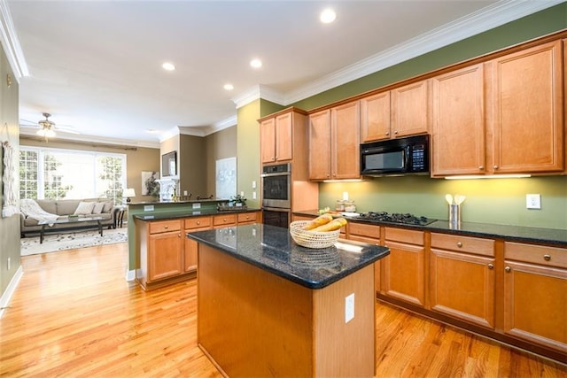 kitchen featuring black appliances, a center island, light wood finished floors, ornamental molding, and open floor plan