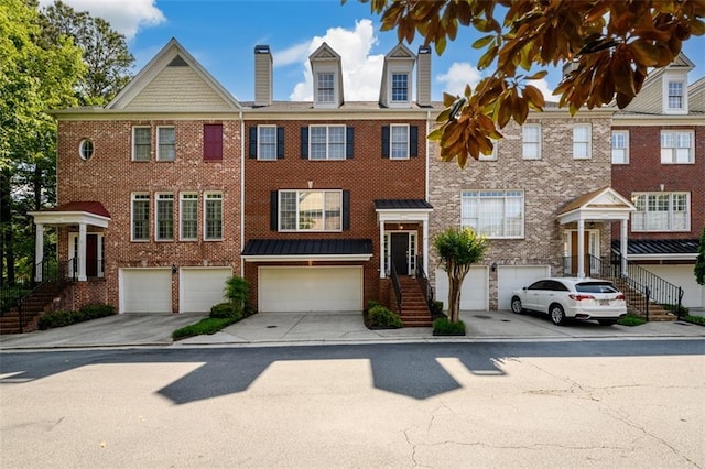 townhome / multi-family property featuring brick siding, an attached garage, driveway, stairway, and a chimney