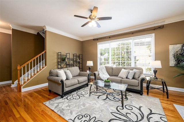 living area with stairway, ornamental molding, baseboards, wood finished floors, and ceiling fan