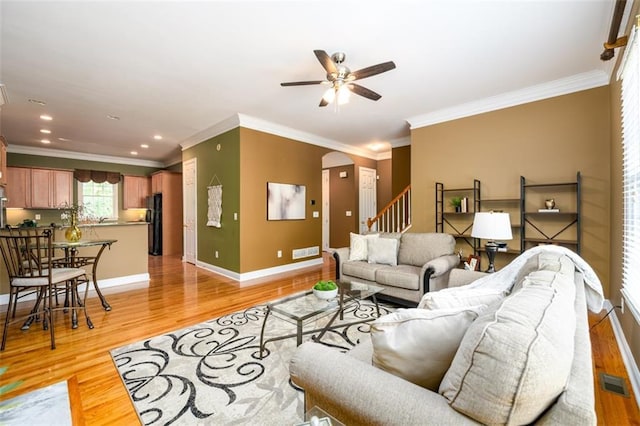 living area with a ceiling fan, light wood finished floors, arched walkways, baseboards, and ornamental molding