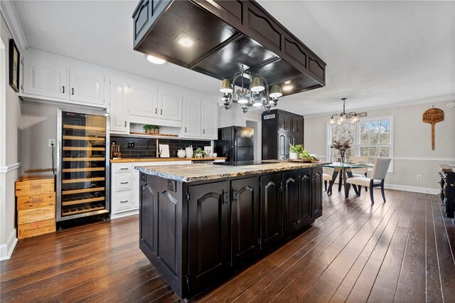 kitchen featuring premium range hood, decorative light fixtures, a center island, beverage cooler, and white cabinets