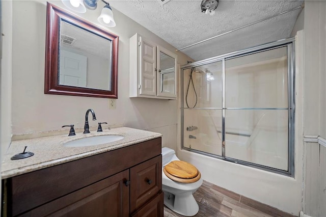 full bathroom featuring wood-type flooring, shower / bath combination with glass door, vanity, toilet, and a textured ceiling