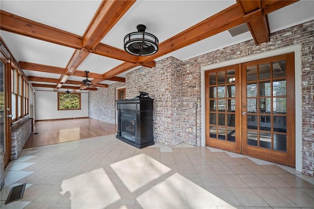 unfurnished living room with light tile patterned floors, ceiling fan, brick wall, french doors, and a wood stove