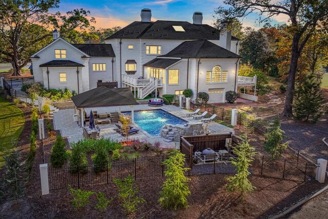 back house at dusk featuring a pool with hot tub, an outdoor living space, a patio area, and a balcony