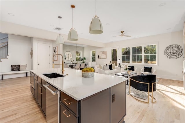 kitchen with a sink, light wood-type flooring, stainless steel dishwasher, and a kitchen island with sink