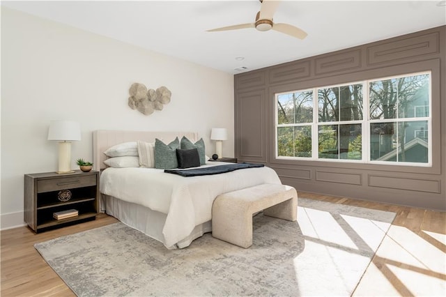 bedroom with light wood finished floors, a decorative wall, and ceiling fan