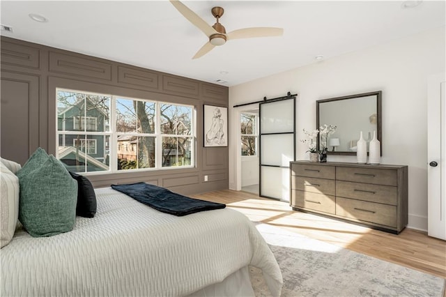 bedroom featuring visible vents, light wood-style flooring, a ceiling fan, and a decorative wall