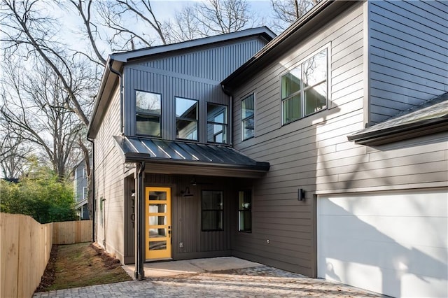 modern home featuring board and batten siding, fence, metal roof, an attached garage, and a standing seam roof