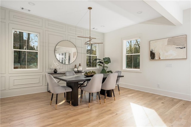 dining room featuring light wood-style flooring, a decorative wall, visible vents, and baseboards