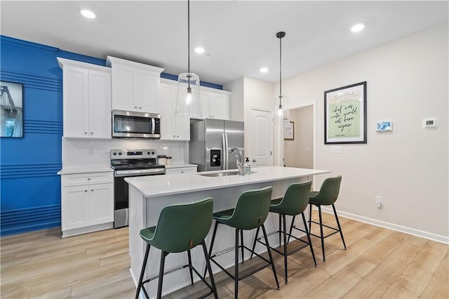 kitchen with hanging light fixtures, a sink, light countertops, stainless steel appliances, and a center island with sink