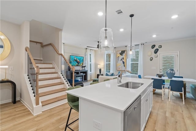 kitchen with a sink, a kitchen island with sink, decorative light fixtures, white cabinets, and dishwasher