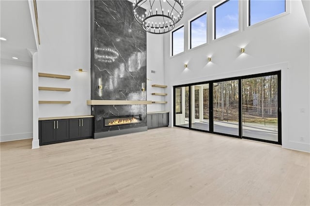 unfurnished living room featuring a wealth of natural light, a towering ceiling, a premium fireplace, and light wood-type flooring