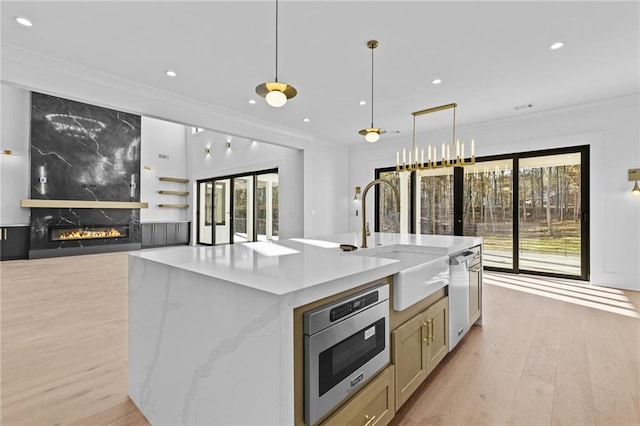 kitchen featuring a center island with sink, a fireplace, hanging light fixtures, and appliances with stainless steel finishes