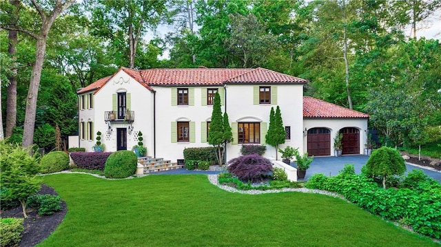 mediterranean / spanish-style home with a balcony, aphalt driveway, a tiled roof, an attached garage, and a front yard