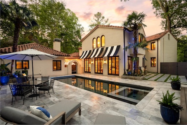 rear view of property with an outdoor pool, a chimney, an in ground hot tub, a tiled roof, and a patio area