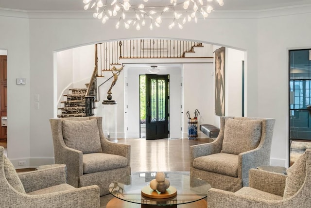 sitting room with ornamental molding, arched walkways, wood finished floors, and stairs