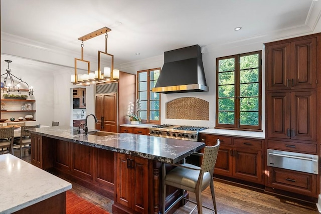 kitchen featuring a center island with sink, wall chimney exhaust hood, paneled refrigerator, a sink, and a warming drawer