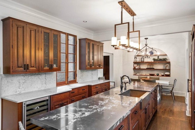 kitchen with light stone counters, wine cooler, decorative light fixtures, a sink, and glass insert cabinets