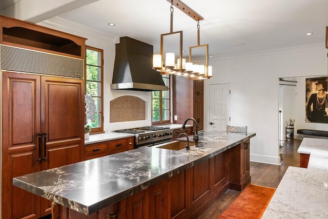 kitchen featuring high quality appliances, ornamental molding, hanging light fixtures, wall chimney range hood, and a sink