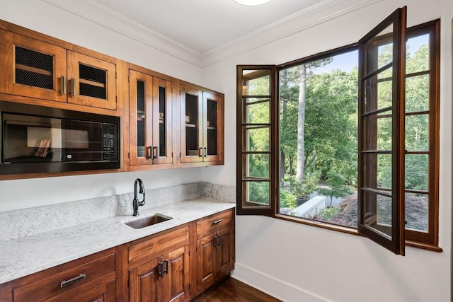 kitchen featuring glass insert cabinets, light stone countertops, crown molding, black microwave, and a sink