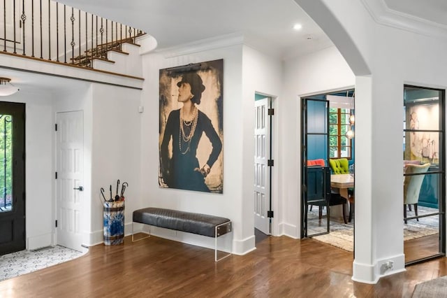 foyer with arched walkways, ornamental molding, wood finished floors, and baseboards