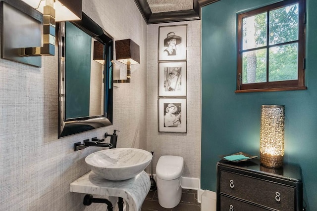 half bathroom with crown molding, a sink, toilet, and tile patterned floors