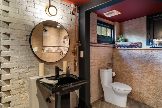 half bath with brick wall, wood finished floors, and toilet