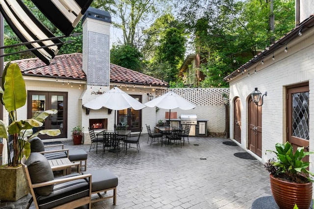 view of patio with an outdoor brick fireplace, a grill, fence, outdoor dining area, and exterior kitchen