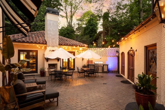 patio terrace at dusk with outdoor dining area, an outdoor kitchen, area for grilling, a fireplace, and fence