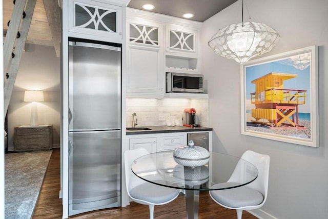 kitchen with white cabinets, dark countertops, glass insert cabinets, stainless steel appliances, and pendant lighting