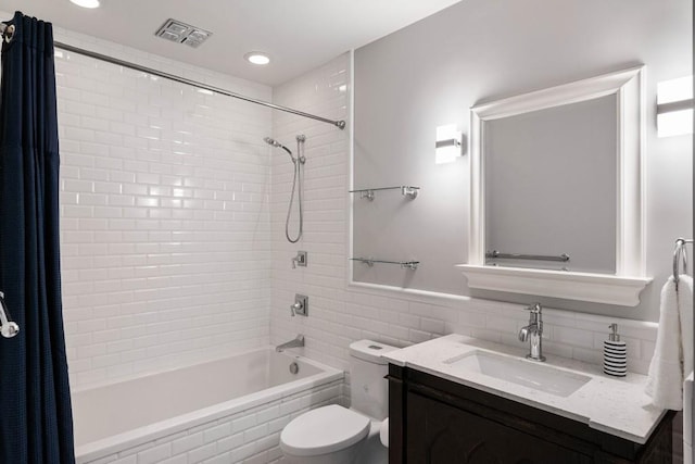 full bath with tiled shower / bath, tile walls, visible vents, toilet, and vanity