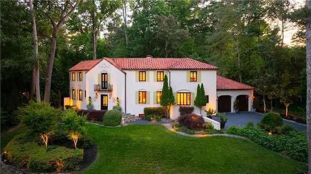 mediterranean / spanish house featuring aphalt driveway, a tiled roof, an attached garage, a front lawn, and stucco siding