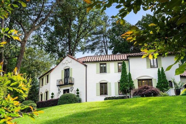 view of front of property with a balcony, a tile roof, and a front yard