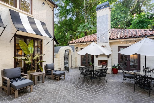 view of patio / terrace featuring a warm lit fireplace, outdoor dining space, and french doors