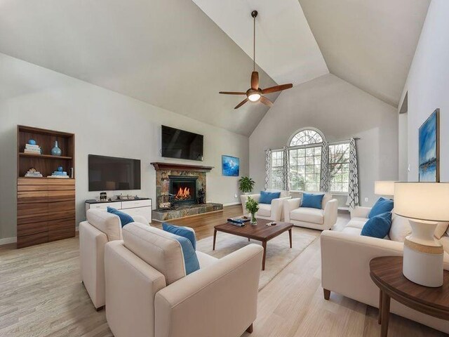 living room with ceiling fan, a stone fireplace, high vaulted ceiling, and light hardwood / wood-style flooring